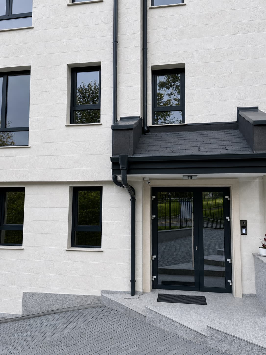 Entrance door with surround, anthracite windows and white bush-hammered flexible stone