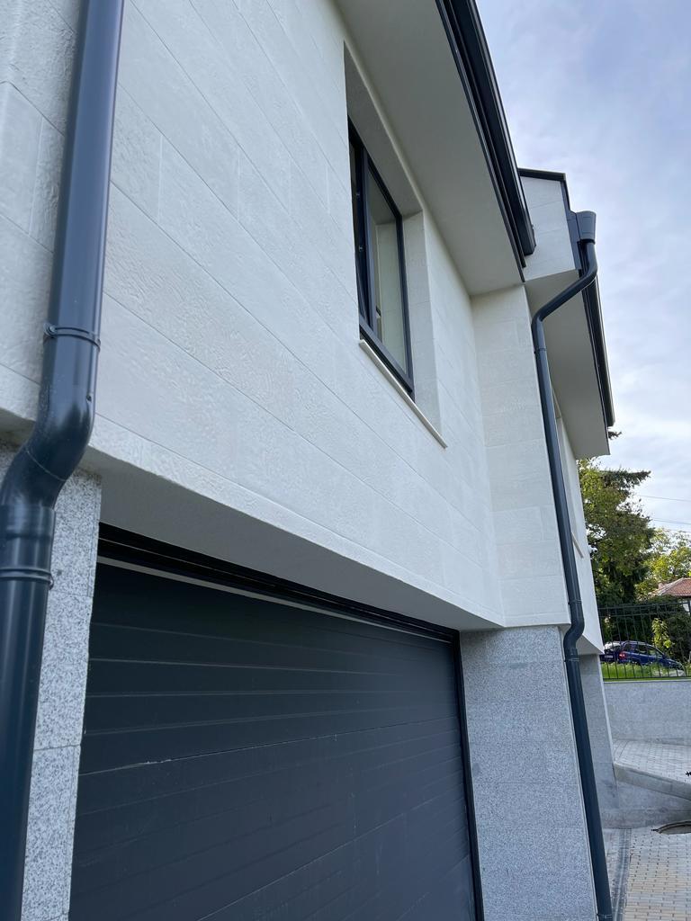 Anthracite downpipe on the white flexible stone corner above the grey garage door