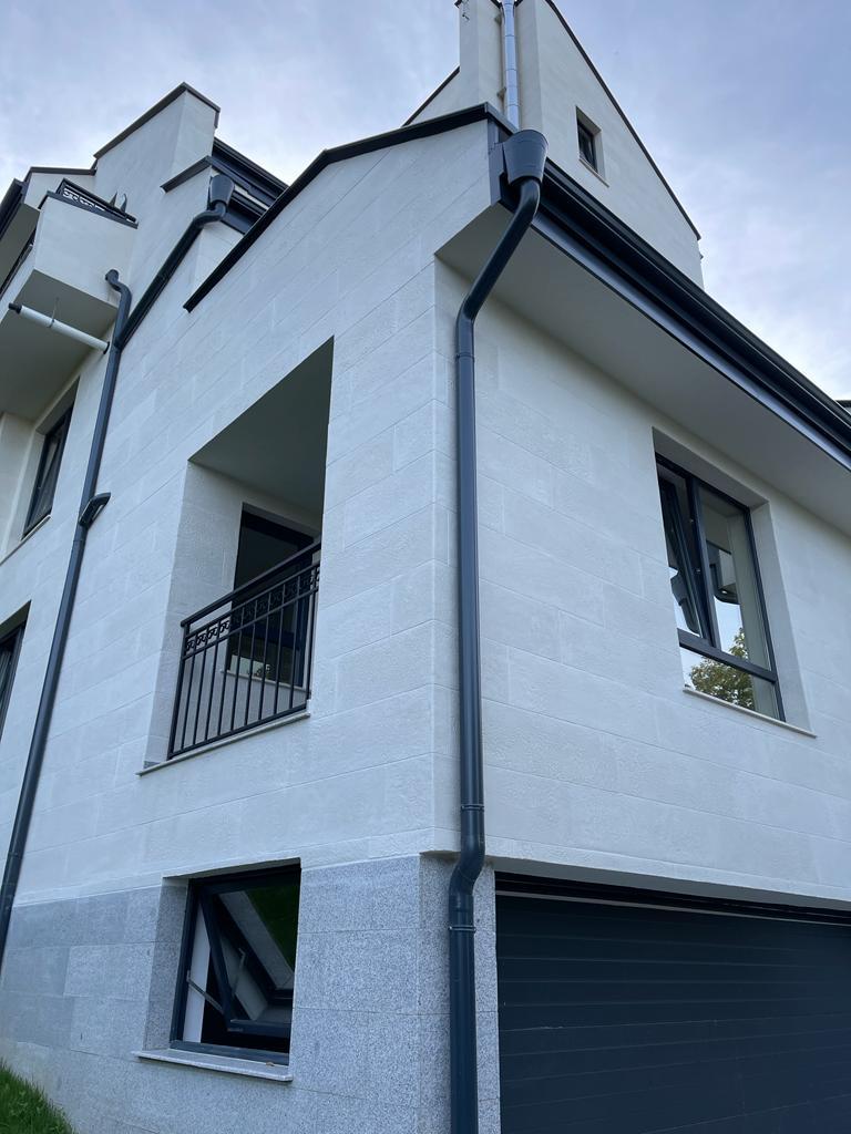 Corner with a balcony and black railing, downpipe and anthracite eaves, white flexible stone from below