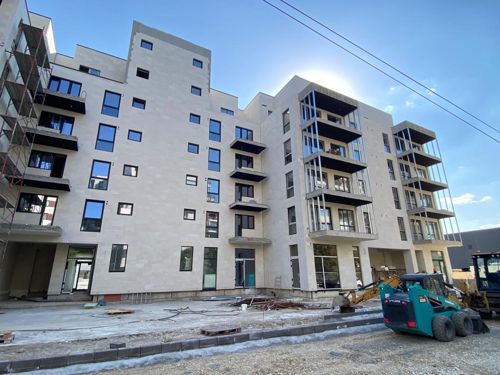 Block with balconies against the sun, clad in beige flexible stone, an excavator on gravel
