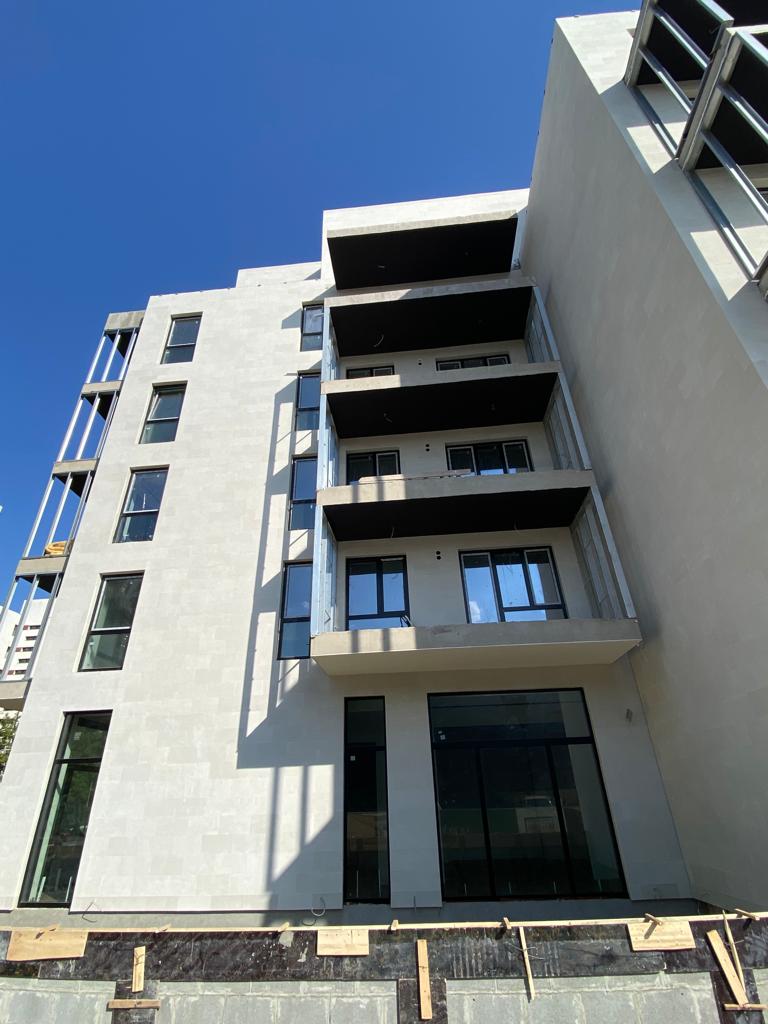 Corner of a block from below: stacked balconies and an anthracite plinth under beige flexible stone