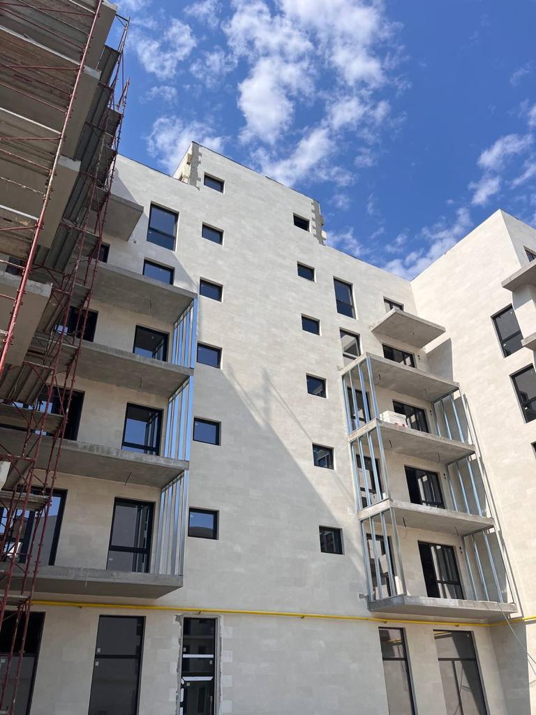Contemporary block from below: scaffolding with red rails and cantilevered balconies in beige stone