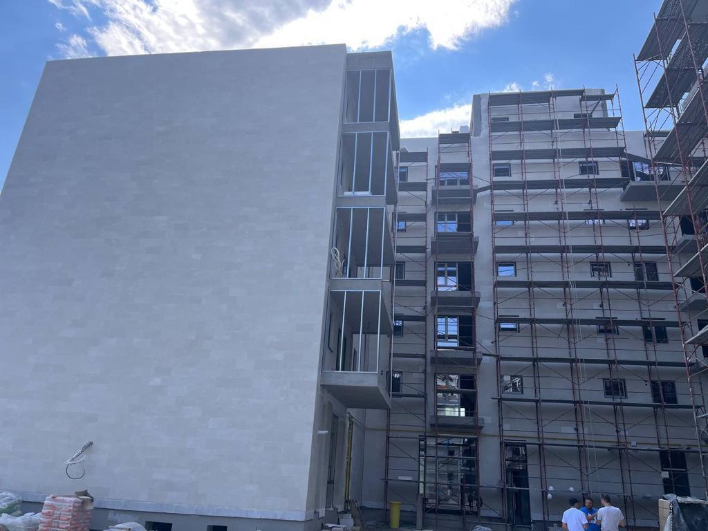 Beige gable wall from below, with a scaffolded block and workers in the background