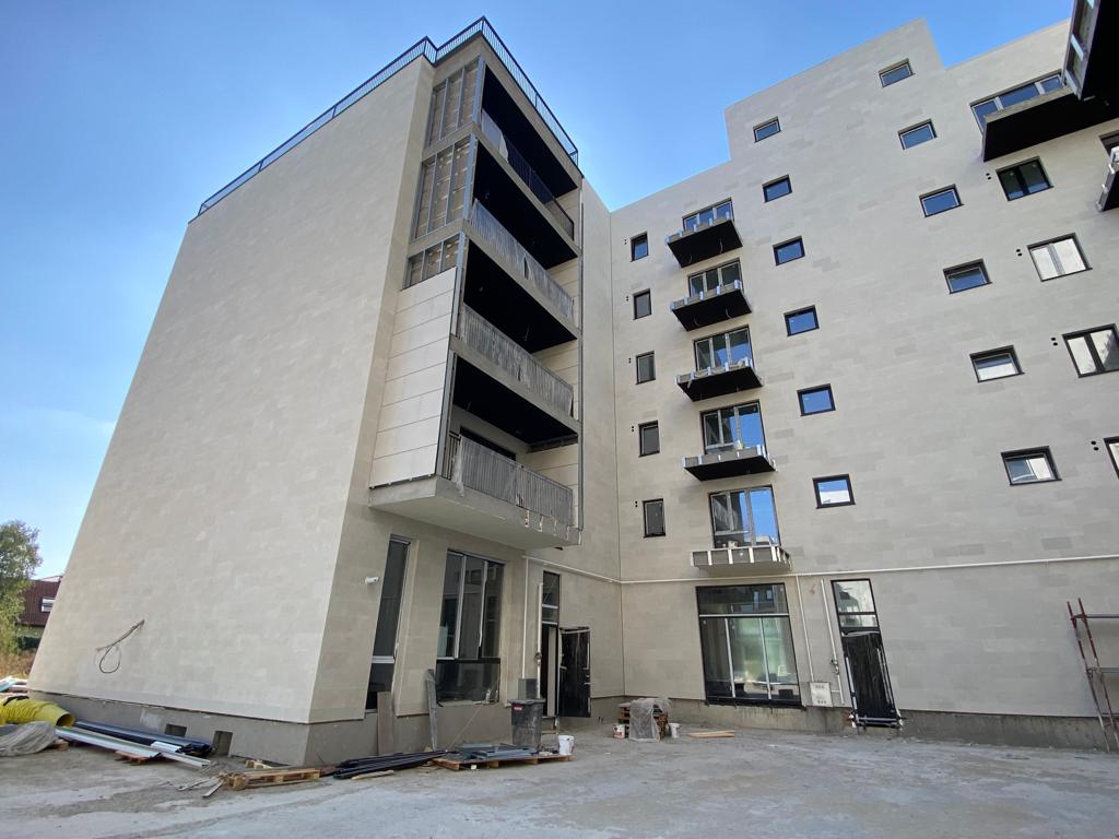 Block with an anthracite-clad stair tower and beige balconies on a construction site