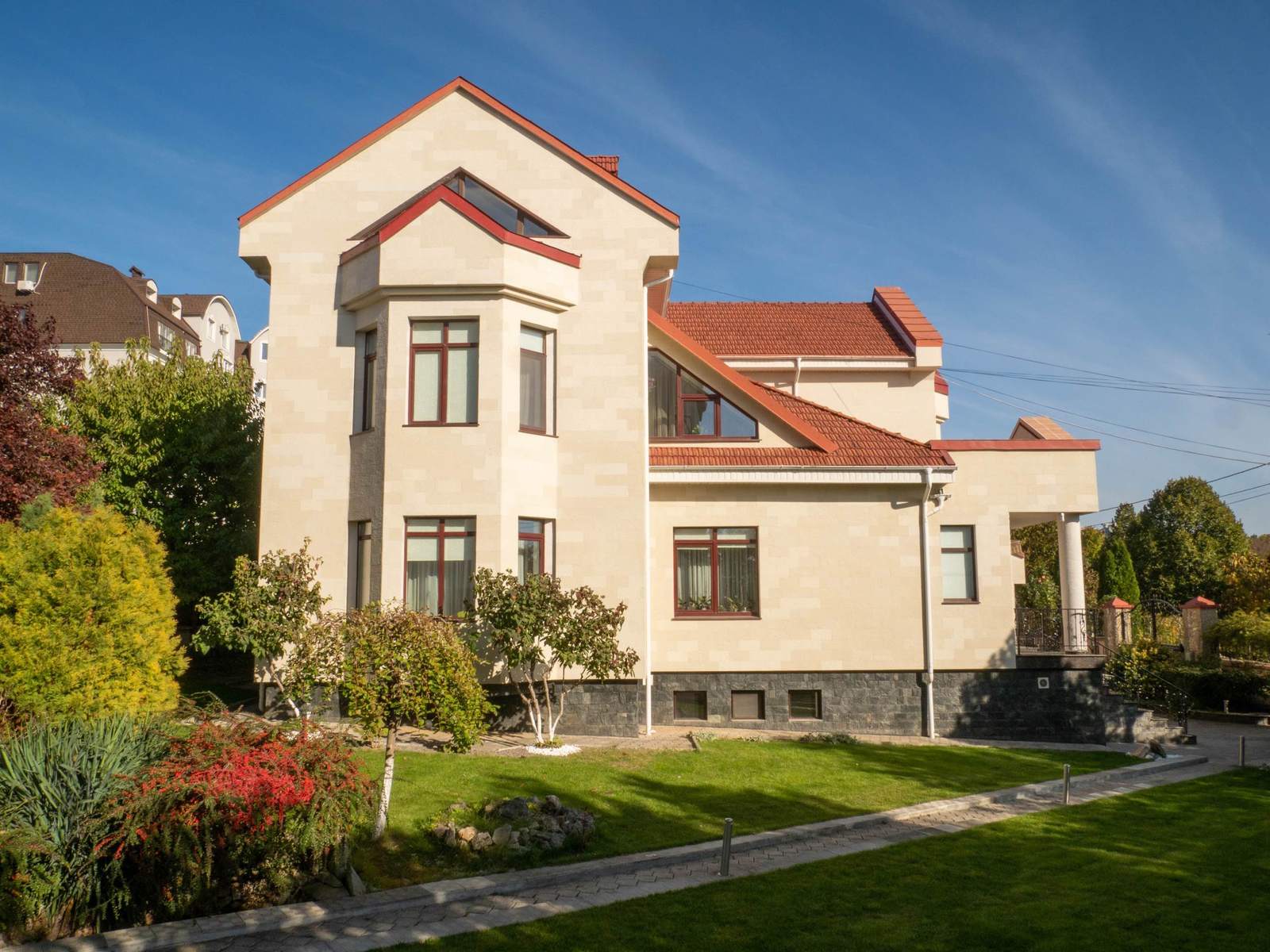 Side view of the house: tall gables, red roof and a Tender Rock flexible stone facade, with lawn
