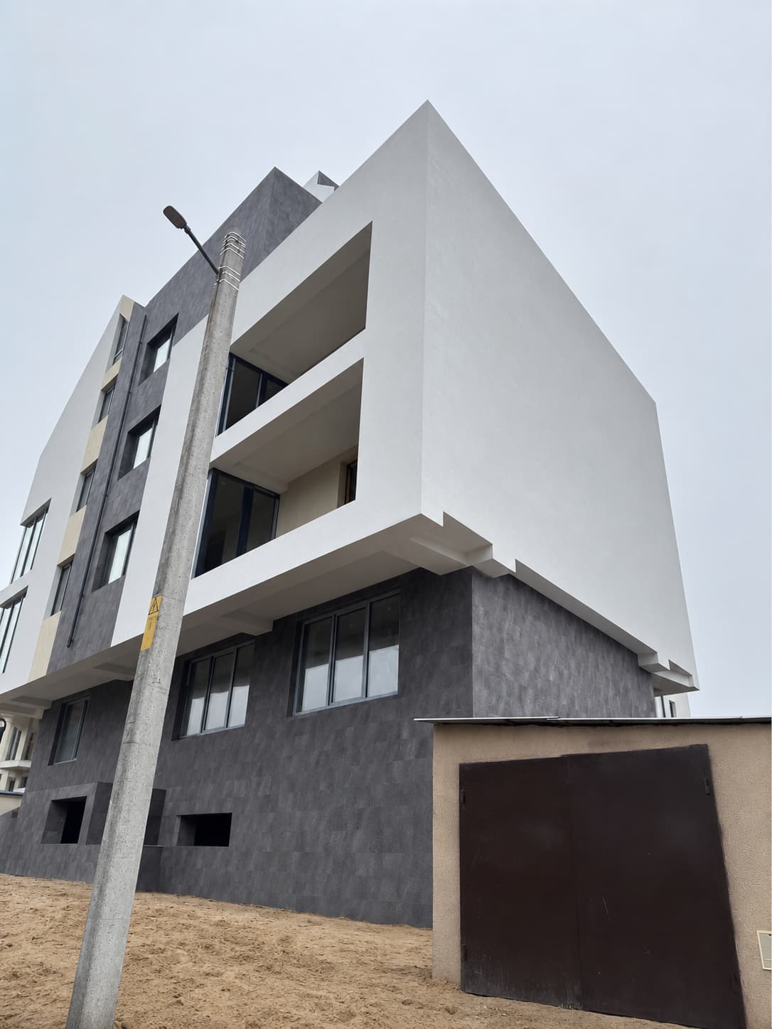 Building corner: white cantilevered volume above the ground floor clad in Royal Granite flexible stone