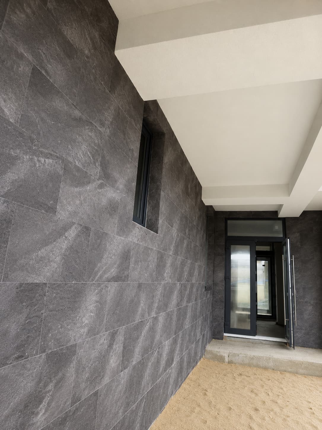 Entrance under the white overhang: Royal Granite wall, narrow window and glass door