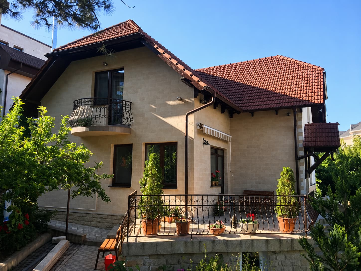 Beige house clad in flexible stone, red tiled roof and wrought-iron balcony