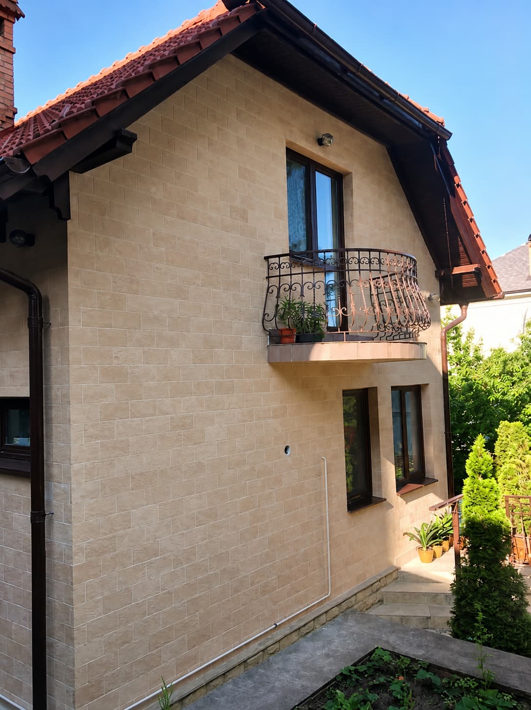 Gable of the house in beige flexible stone, wrought-iron balcony and half-bond tile pattern
