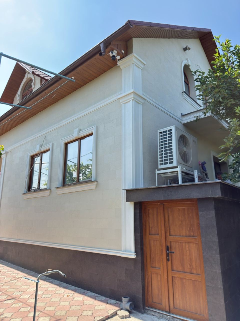 House corner in light flexible stone, white cornice, two windows and a wooden door, dark plinth