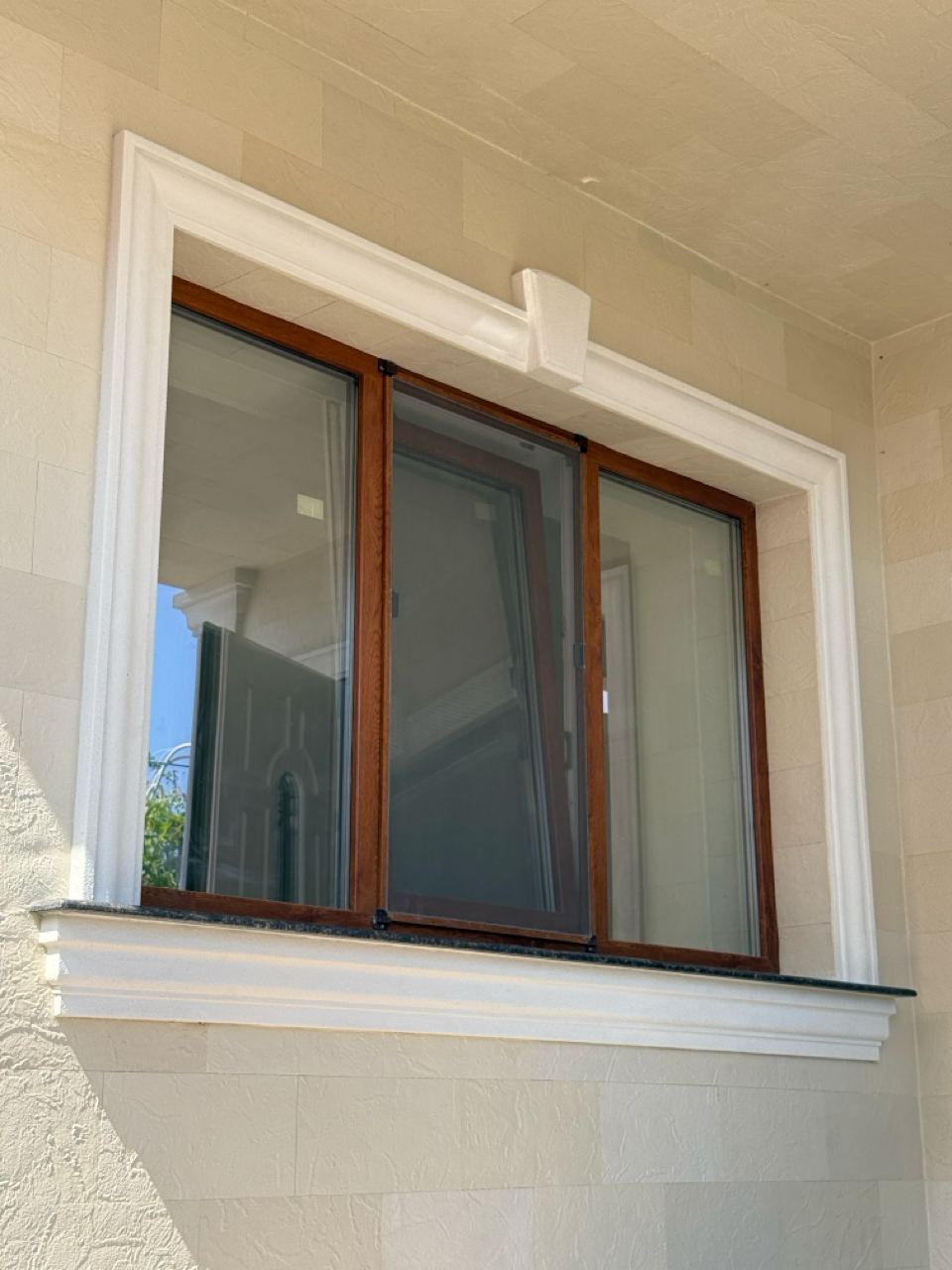Window with a wooden frame and white surround, framed by light flexible stone