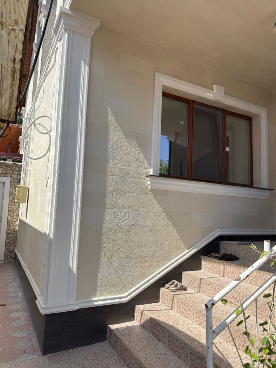 Window with a white surround by the entrance steps, light flexible stone wall and dark plinth