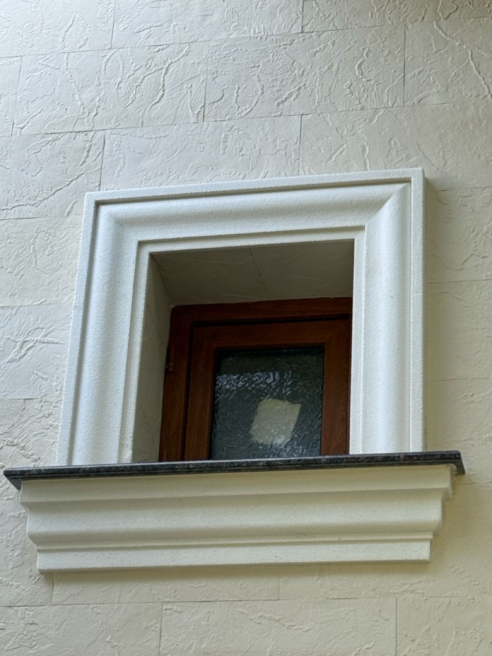 Small window with a white surround and sill, fine-textured flexible stone wall