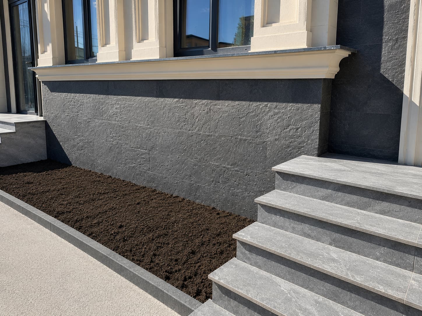 Anthracite split-face plinth, grey stone steps and a beige cornice above a freshly prepared bed