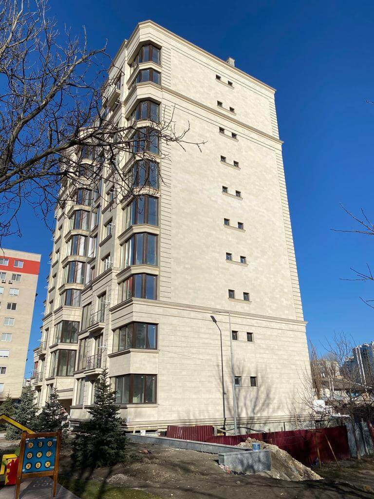 Ten-storey residential block clad in beige flexible tile, bay windows and cornices between levels