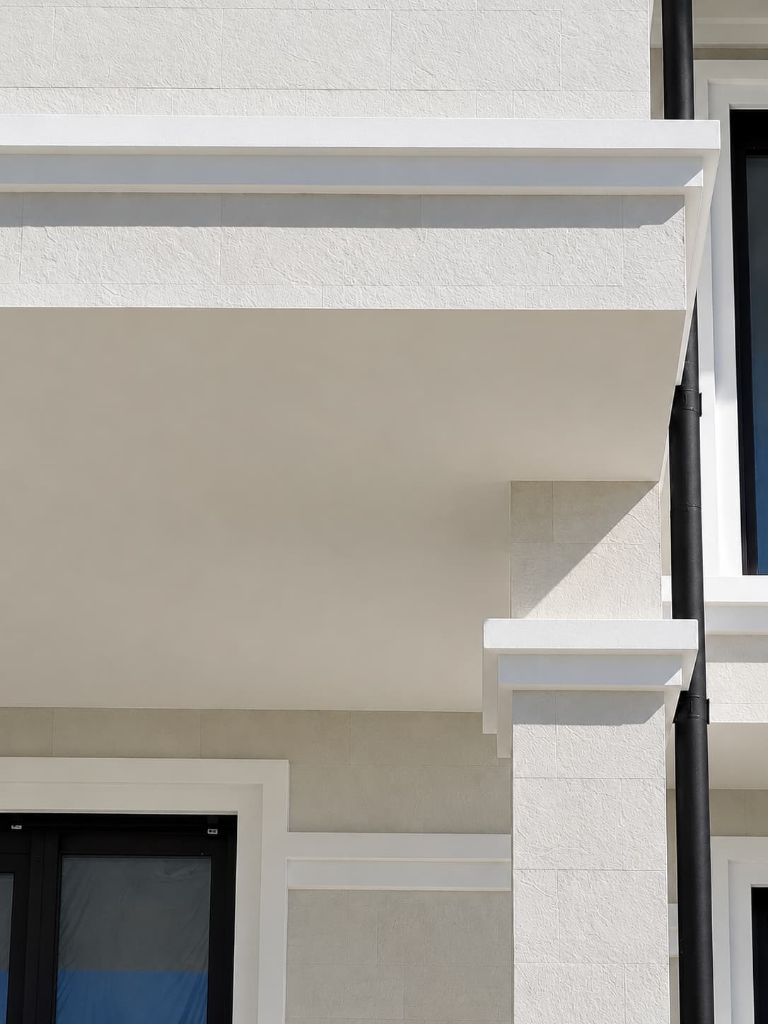 Wall under a white cornice with a black window and a flexible stone corner, seen from below
