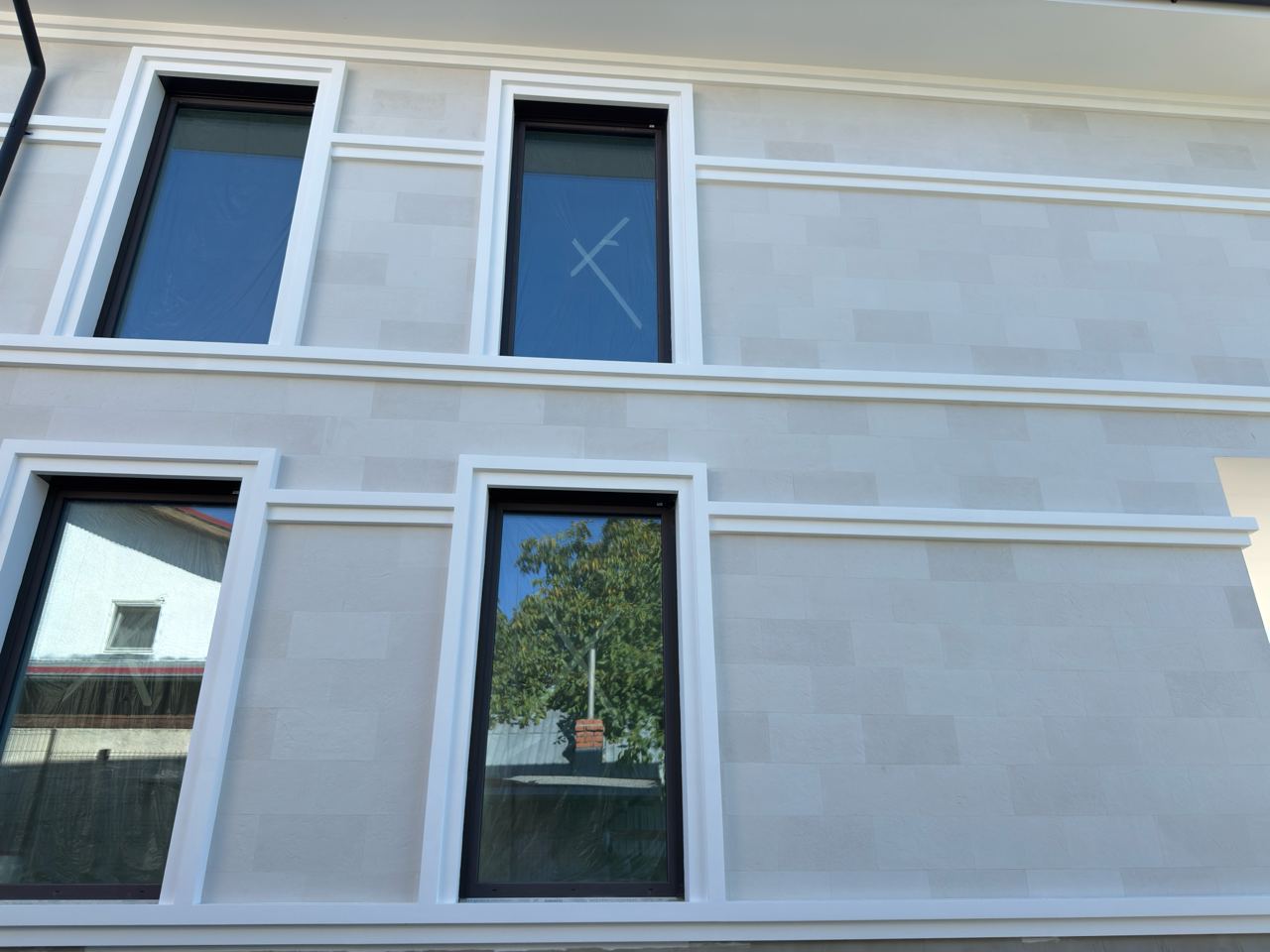 Side facade with four windows in white surrounds and a white belt, clad in light flexible stone